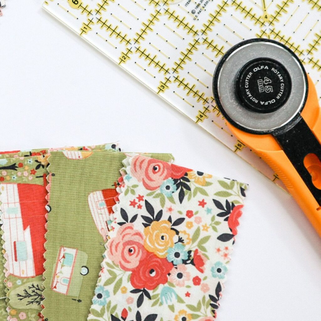 A ruler, rotary cutter and strips of green floral fabric arranged on a table.