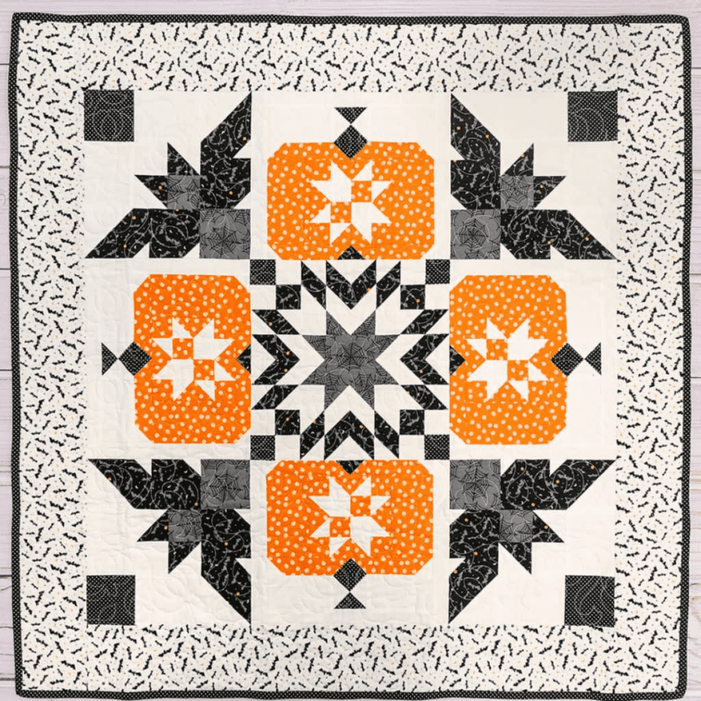 A quilt with bats, pumpkins and a spider web.
