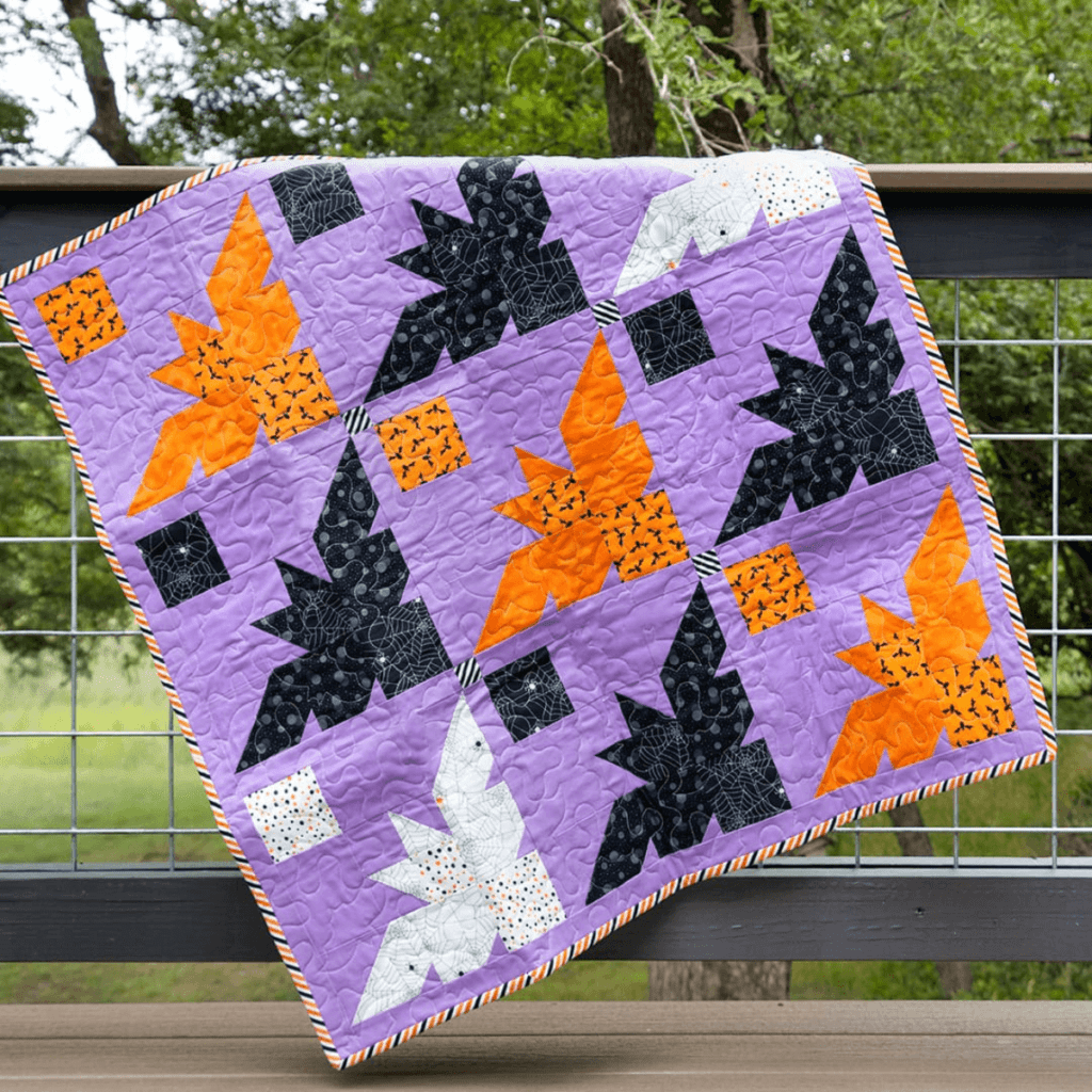 A purple quilt with white, black and orange bats.