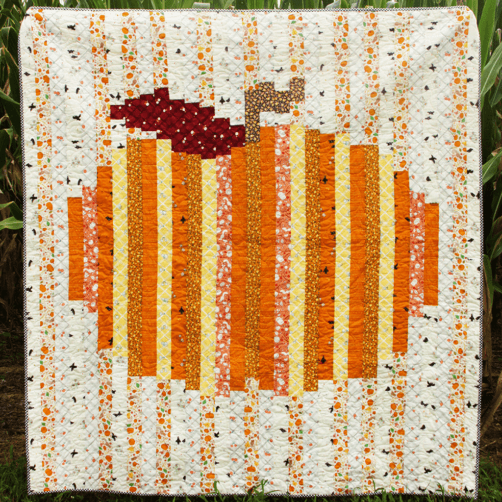 A quilt with an orange pumpkin made from strips of fabric.