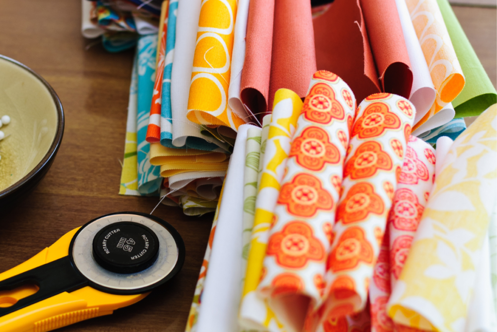 Fabric stacks lined up and a rotary cutter on a table.