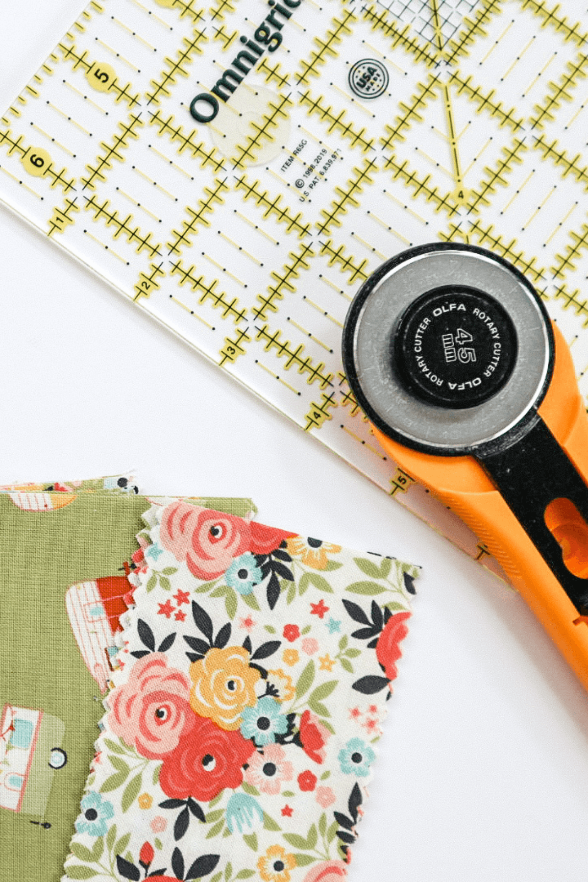 A rotary cutter, ruler and strips of green floral fabric.